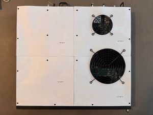 This was sizing attempt 4 of 5. I cut a lot of paper that week. A top-down view of a rack-mount network switch, the Brocade ICX 7450-24, on a table, but with the top covered by 4 equal squares of printer paper, cut as templates for the replacement panels being designed.